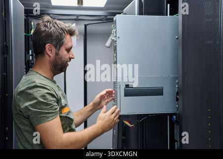 IT technician inspecting and installing server hardware inside a data center equipment rack Stock Photo
