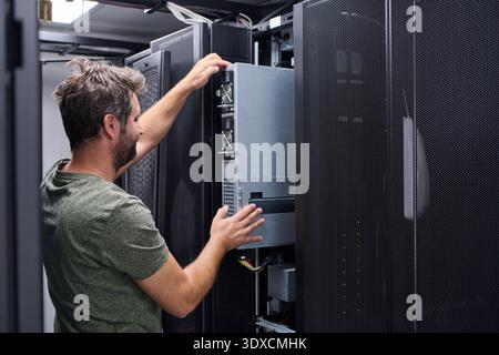 Server technician installing a rack server in a modern data center performing IT maintenance and hardware upgrade Stock Photo