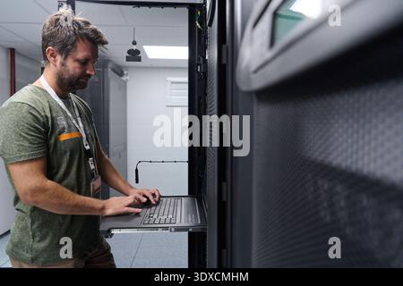 IT technician working on server rack with laptop in a modern data center server room Stock Photo