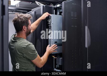 IT technician installing server hardware in a data center rack performing maintenance and configuration Stock Photo