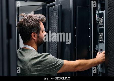 It technician checking servers in a data center rack performing hardware maintenance and network troubleshooting Stock Photo