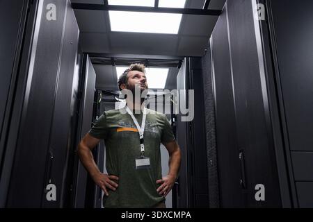 Confident IT technician inspecting server racks in a modern data center with hands on hips Stock Photo