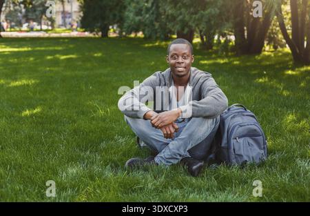 Man Sitting on Grass in a Park With a Backpack Enjoying the Outdoors During the Day Stock Photo