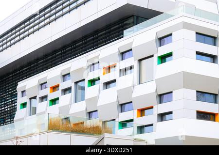 The exterior of a contemporary building showcases a unique facade design featuring repeating geometric shapes and vibrant orange and green window fram Stock Photo