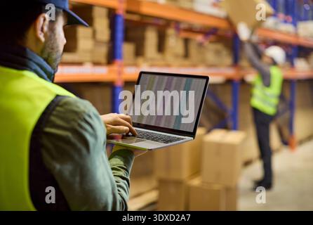 Warehouse inventory with worker using laptop to track stock on shelving racks Stock Photo