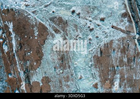 Icy marshland creek naturally bisecting fields of dry brown reeds and winter grasses. Aerial drone perspective. The striking contrast of frost forms an exceptional environmental wallpaper. Stock Photo