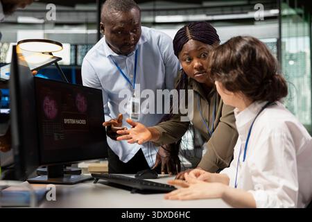 Startup office programmer doing software debugging, helped by coworkers to fix malware. IT worker fighting hacker ddos attack, being assisted by team members sharing helpful advice Stock Photo