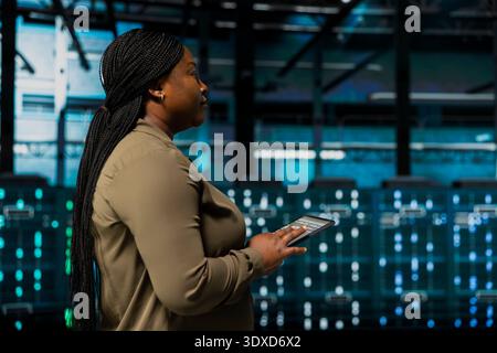 Close up of software developer using device to do maintenance in data center with setup helping companies stay connected. IT specialist walks with tablet between server hub rigs blinking lights Stock Photo