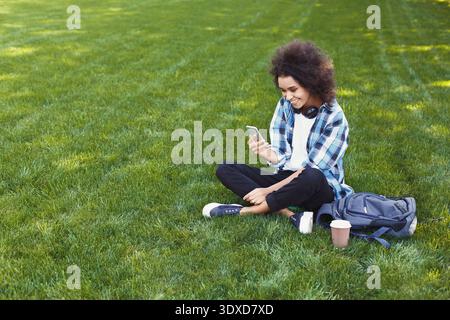 Young Person Sits on Grass While Using Smartphone in a Public Park During Afternoon Hours Stock Photo