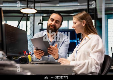 Lead technician providing support to new employee in software development agency using tablet. Seasoned IT expert using device to present best practices to trainee during internship in tech startup Stock Photo