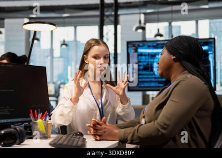 Junior dev and female programmer gossiping about coworkers, having fun. Group of women engaged in workplace chat during job shift break, exchanging office news about colleagues Stock Photo