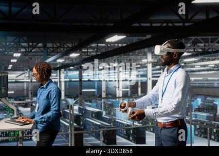 African american AI engineer uses VR headset to monitor neural network systems. Server room IT expert using virtual reality tech to oversee equipment powering machine learning processes. Stock Photo