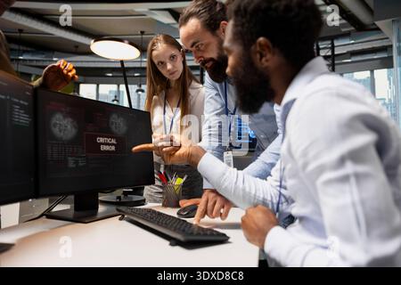 Team of engineers in office surprised by critical error warning popup, struggling to fix it. Teamworking IT experts doing brainstorming, troubleshooting error notification on PC screen Stock Photo