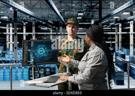 Army tech expert in data center presenting tactical options to commander based on predictive AI models analysis. Server farm workers reading artificial intelligence reports Stock Photo