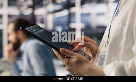 Close up of data center system administrator coding on tablet, doing software updates. Server room IT expert looking at device screen, optimizing infrastructure rackmounts configuration rigs, camera A Stock Photo