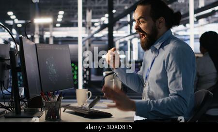 Server room IT specialist frustrated by difficult complex tasks in office. Stressed engineer developing neural network software while working extended hours in data center, camera A Stock Photo