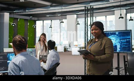 Happy female engineer in office automating repetitive tasks using AI scripts. Jolly african american developer using artificial intelligence to speed up feature implementation, camera A Stock Photo