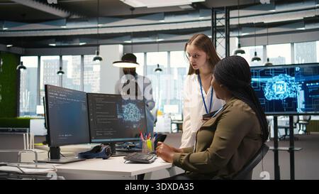 Smiling startup manager teaching junior dev how to use machine learning tech. Happy african american team leader showing intern in office how to use AI predictive models, camera A Stock Photo