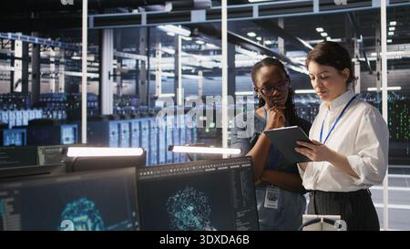 Teamworking engineers in data center integrate AI automation tools together during maintenance session. Server room colleagues configure machine learning models across server infrastructure, camera A Stock Photo