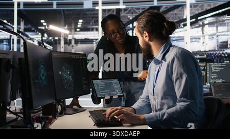 Teamworking system administrators in data center integrating AI automation during maintenance session. Server farm coworkers configuring machine learning models across equipment rigs, camera A Stock Photo