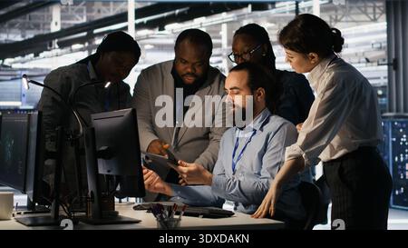 Data center system administrators performing maintenance on supercomputers used for AI processing. Team managing server hub rigs used for deep learning training, looking over business charts, camera A Stock Photo