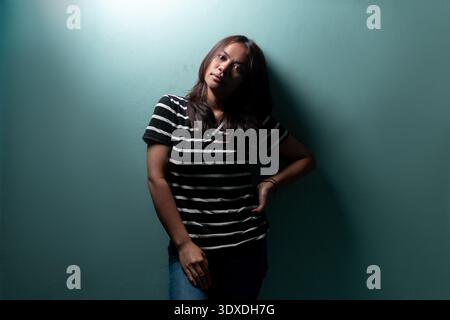 Portrait of a young Indonesian woman in a striped shirt. High-contrast studio lighting for concepts of female strength, mystery, and modern lifestyle. Stock Photo