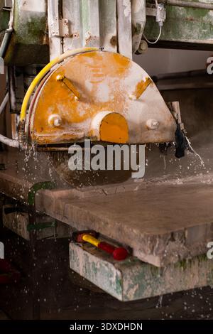 A diamond blade rotating disc in a marble cutting saw is operating in a stone water processing plant. The machinery, with a prominent yellow protectiv Stock Photo