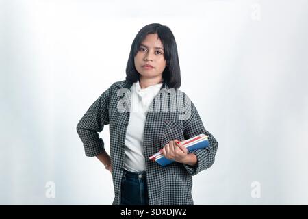 A confident Indonesian woman holding colorful notebooks in a studio. Clean portrait on white background, ideal for education and campus life concepts. Stock Photo