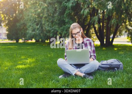 Student Works on Laptop While Sitting on Grass in Park During Sunny Day Stock Photo