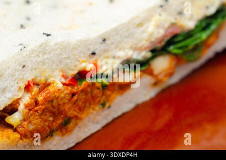 A sandwich with a variety of ingredients including meat, cheese, and greens. The sandwich is cut in half and placed on a white plate Stock Photo