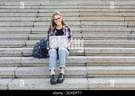 Young Person Sits on Steps Using Laptop to Work on School Tasks or Projects Stock Photo
