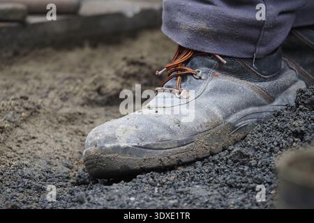 Construction worker stands on dirt with muddy boots Stock Photo