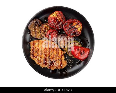 Grilled meat and assorted vegetables on a black plate. Isolated on white background, top view. Stock Photo