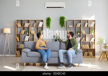 Couple controlling air conditioner with remote in cozy modern home living room Stock Photo