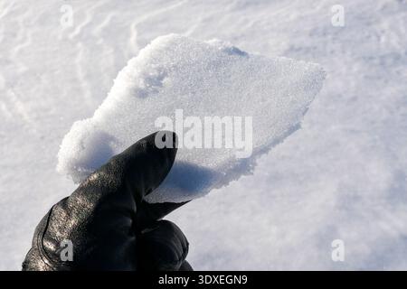 Close-up of a gloved hand holding a piece of fresh snow under bright winter sunlight. Stock Photo