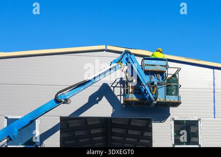 Construction Worker on Hydraulic Lift Installing Roof Panels on Industrial Building Stock Photo