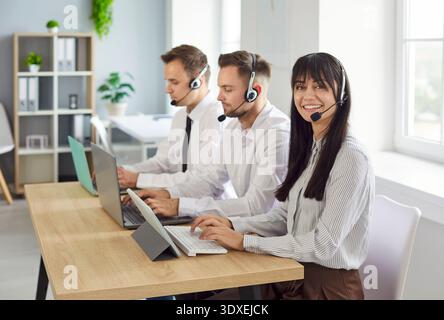 Smiling call center team with headsets working at laptops in bright office Stock Photo