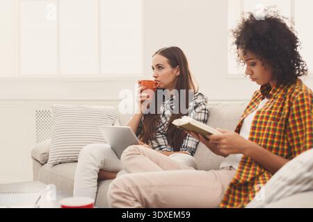 Two People Relax on a Couch While One Drinks Coffee and the Other Reads a Book Stock Photo