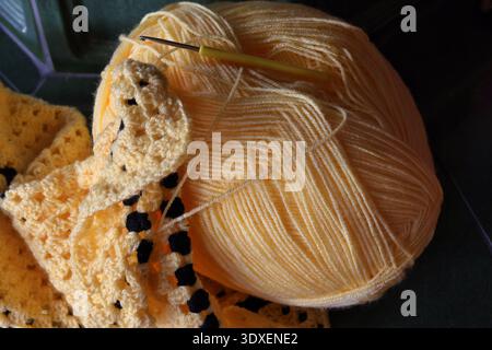 Top view of a large yellow ball of yarn with a crochet hook and a crocheted blanket Stock Photo