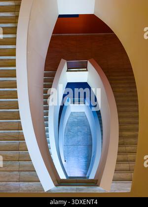 Overhead view of modern curved staircase and geometric spiral architecture, clean lines, symmetry, marble steps, blue accents. Stock Photo