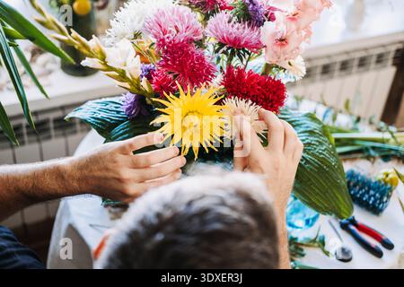 Hands of man arrange vibrant yellow and pink flowers in large white urn. Color therapy, vibrant floral palette, mood-enhancing decor, psychological Stock Photo