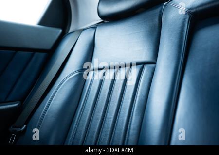 Close-up of a luxury vehicle's navy blue leather interior, featuring elegant vertical ribbed stitching and a seatbelt. Low, wide angle view, no people Stock Photo