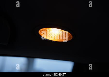 Description: A close-up shot of an oval amber reading lamp located on the interior ceiling of a vehicle, providing warm illumination for passengers. Stock Photo