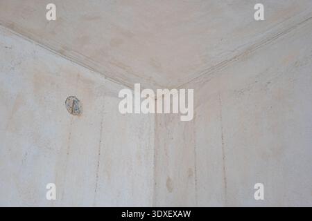 A wide shot of an interior corner during renovation, featuring unfinished light-colored plaster on the walls and ceiling with a recessed electrical ju Stock Photo