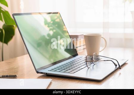 Laptop, eyeglasses, coffee, and books on a desk, creating a productive home office and remote workstation setup. Remote work concept Stock Photo