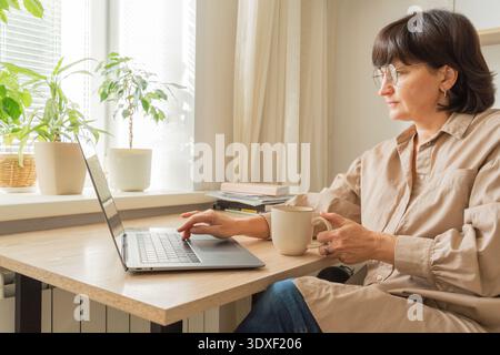 Woman working with laptop from home, drinking coffee Stock Photo