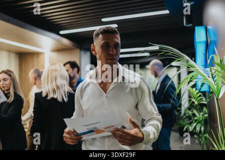 Business professional man in white shirt holding documents in office with colleagues during a busy event Stock Photo