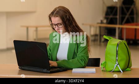 A focused schoolgirl works quietly on a laptop at a desk, warm indoor light and clean composition with copy space. This image connects to online study Stock Photo