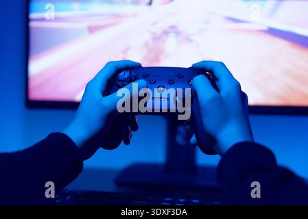 Close up of hands holding game controller while racing video game with motion blur effect plays on widescreen monitor Stock Photo