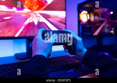 Teen gamer playing racing video game on desktop computer with colorful RGB lights and illuminated gaming PC case Stock Photo